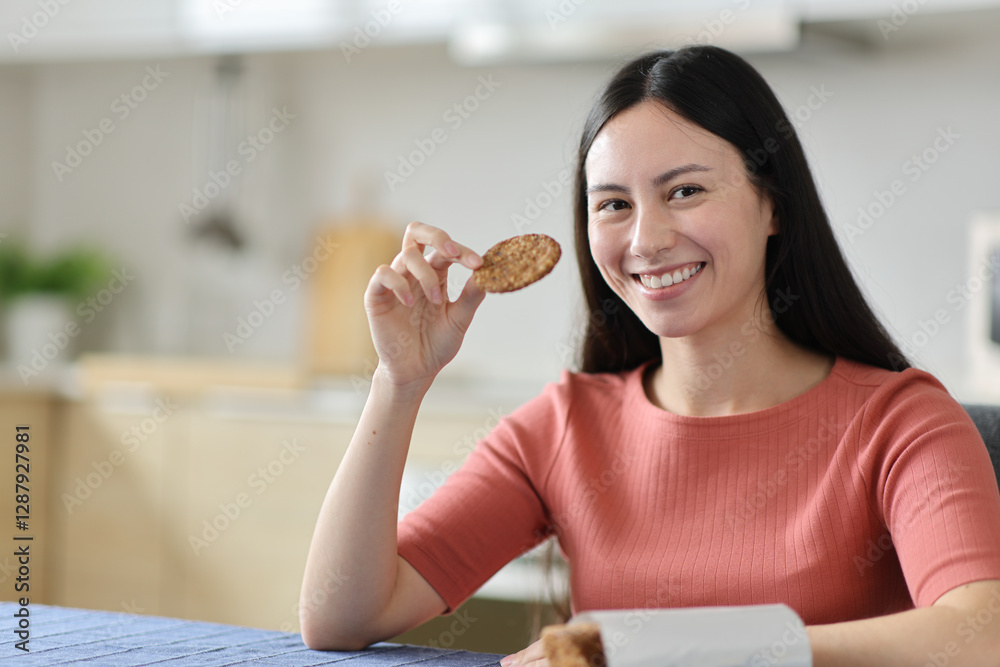 Happy asian woman eating cookies looking at you Happy asian woman eating cookies looking at you
