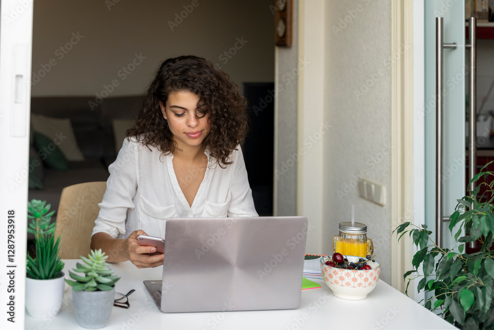 Young woman using cell phone and laptop at desk Young woman using cell phone and laptop at desk