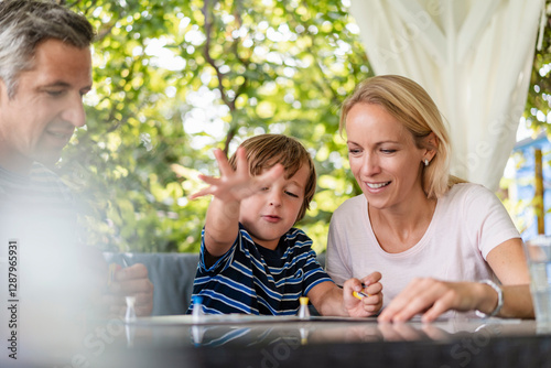Happy parents and son playing a board game on terrace