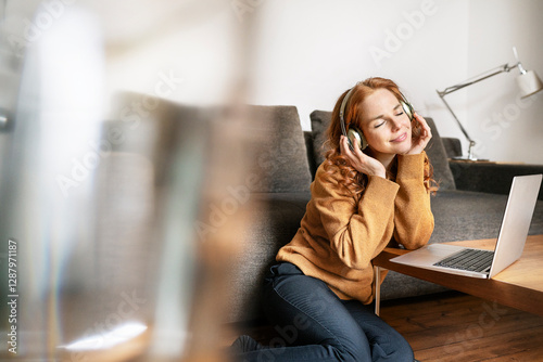 Beautiful woman listening music through headphones while sitting by laptop on coffee table at home