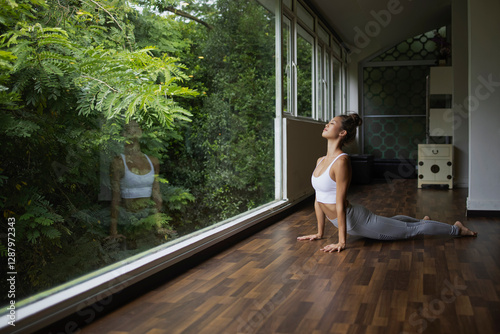 Woman practicing cobra pose in a yoga studio with a view of greenery photo