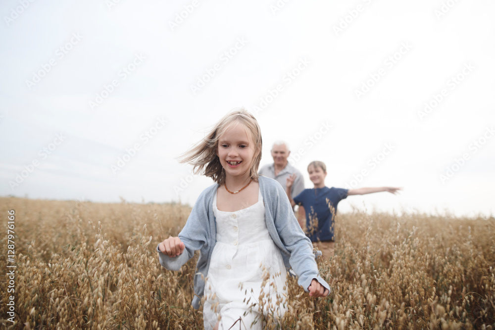 Portrait of happy girl running in an oat field while brother and grandfather following her Portrait of happy girl running in an oat field while brother and grandfather following her