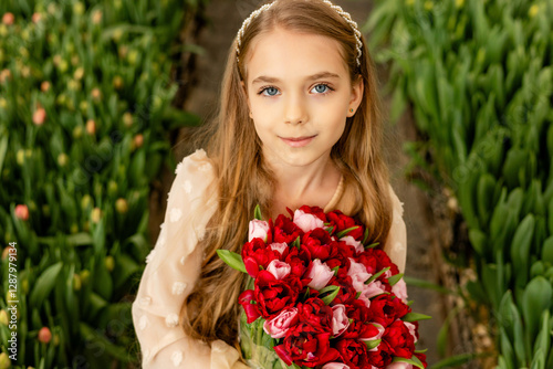 A cute charming girl in a light dress holds a bouquet of red tulips in a greenhouse. Women's day photo