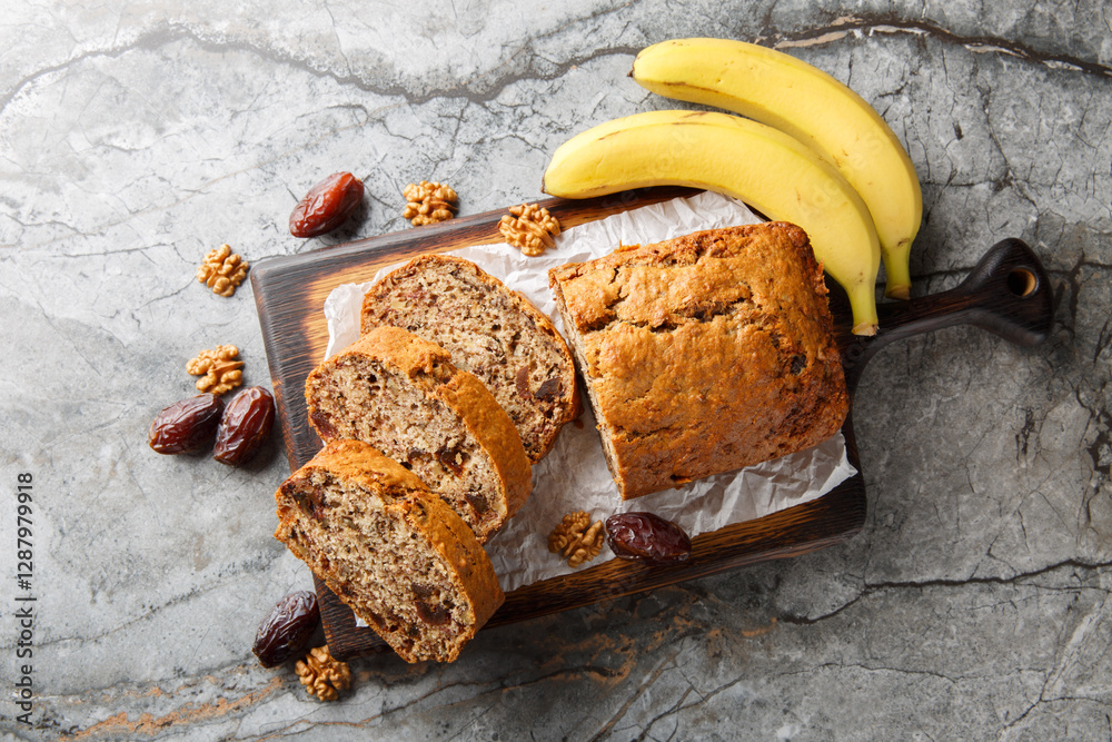 Freshly baked date banana walnuts bread loaf surrounded by ingredients close-up on wooden board on table. Horizontal top view from above