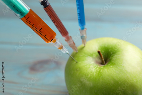 GMO concept. Green apple with syringes on blurred background, closeup