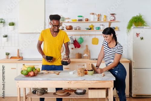 Multiethnic couple breakfasting together in the kitchen, woman using tablet photo