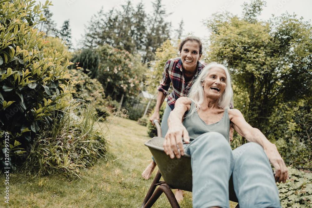 Daughter pushing mother, sitting in push cart, through the garden