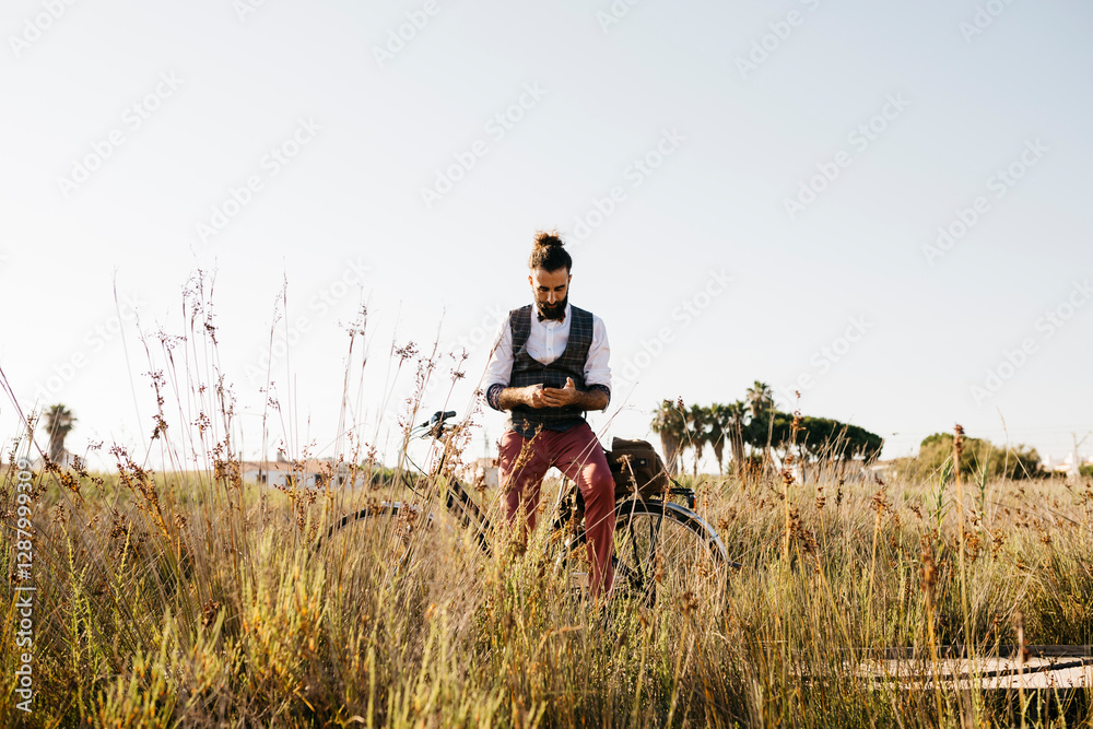Well dressed man with his bike on a wooden walkway in the countryside using cell phone Well dressed man with his bike on a wooden walkway in the countryside using cell phone