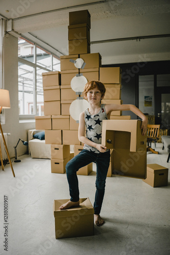 Portrait of redheaded boy playing astronaut standing in front of rocket built of cardboard boxes photo