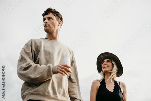 Young couple having a drink outdoors looking sideways