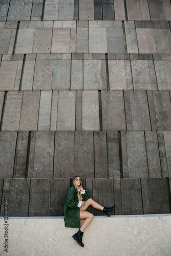 Blond young woman wearing green jacket sitting on a wall, Vienna, Austria photo