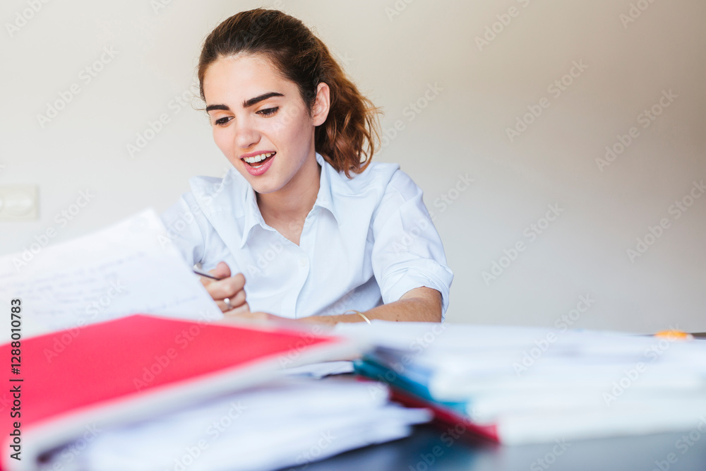 Smiling female student reading document at desk at home Smiling female student reading document at desk at home
