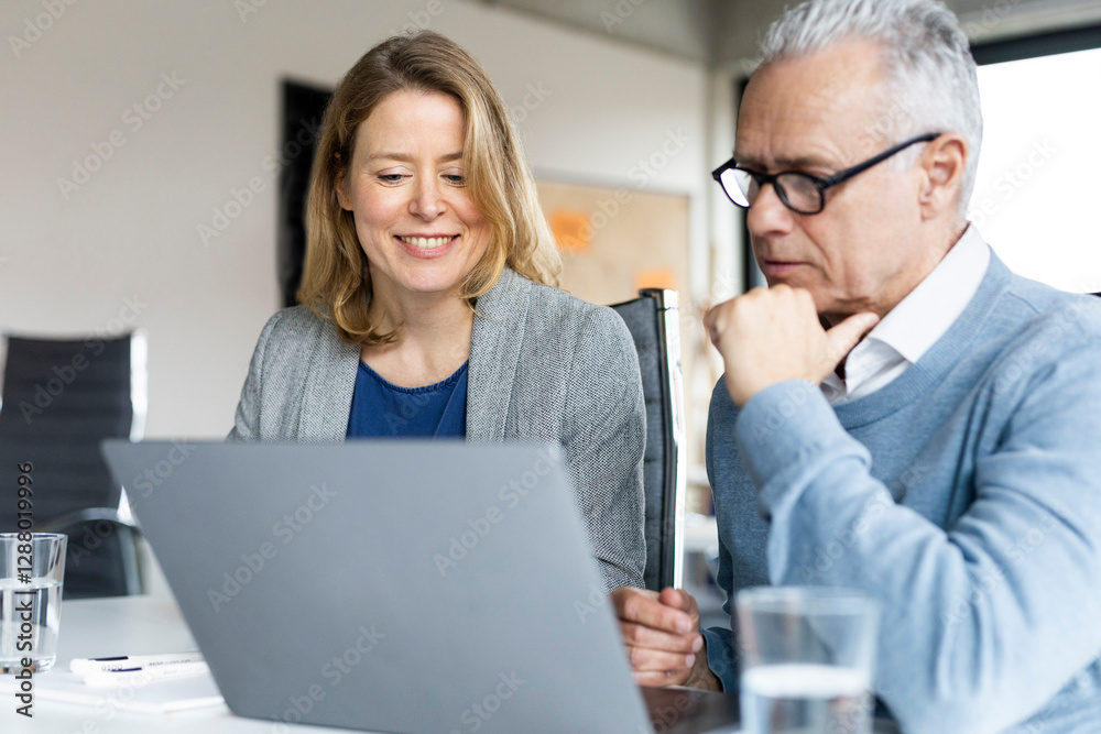 Smiling blond businesswoman with colleague using laptop at office Smiling blond businesswoman with colleague using laptop at office
