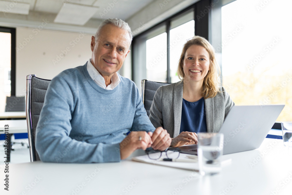 Smiling businessman and businesswoman sitting at table in office Smiling businessman and businesswoman sitting at table in office