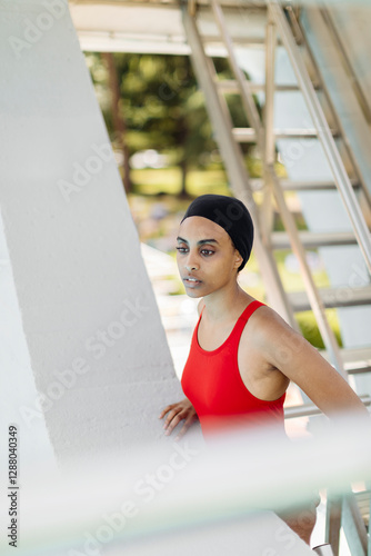 Portrait of young woman wearing swimming cap and red bathsuit standing on stairs of highboard photo