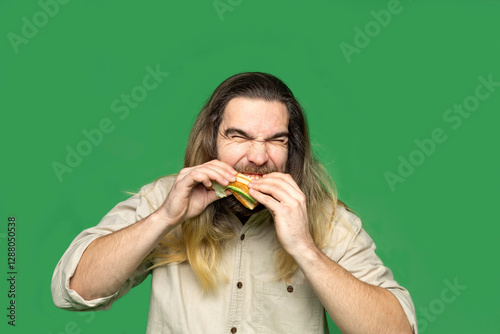 Portrait of bearded man eating sandwich in front of green background photo