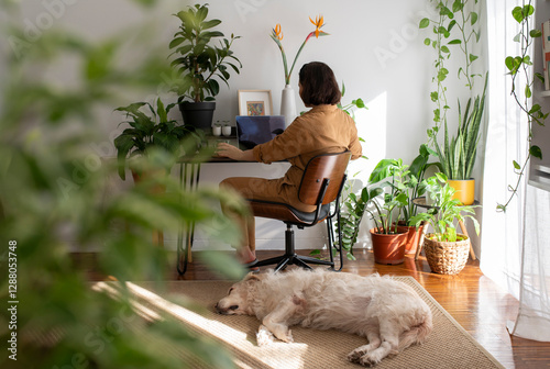 Woman working on a laptop at home in Portugal with a golden retriever and green plants in the living room