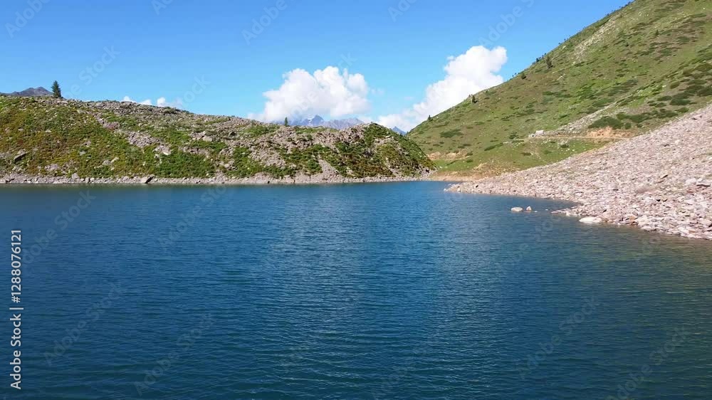 Rama Lake is reflecting the colors of a beautiful blue sky with some fluffy clouds and surrounded by green hills, rocks and mountains in Skardu Valley, Gilgit-Baltistan, Pakistan, drone footage