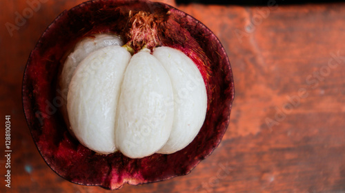 Ripe mangosteen fruit , revealing its juicy white segments inside the dark purple rind.