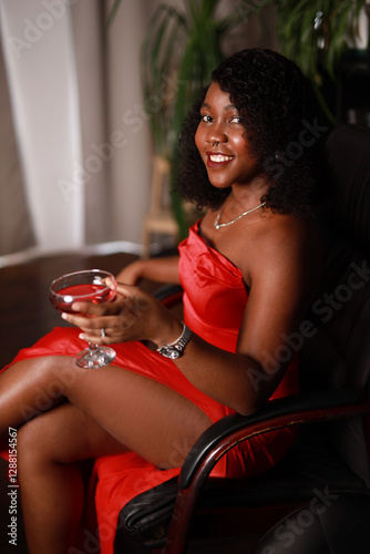 glamorous african woman in red dress with glass of champagne sitting in chair	