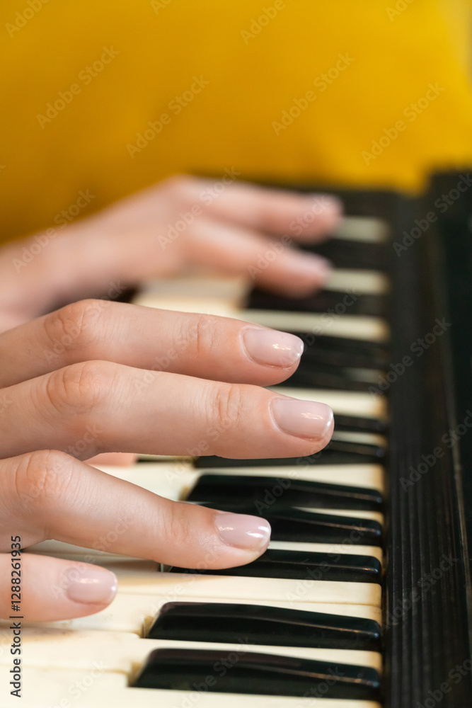 Obraz premium Close-up of female hands playing a synthesizer, creating music in a cozy home or professional studio setting with a yellow sofa in the background, evoking a creative and artistic atmosphere