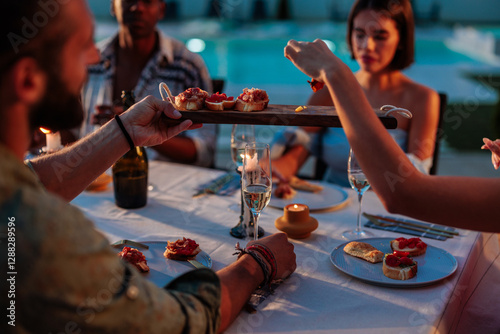 Fotografie Friends sharing appetizers during a luxurious dinner by the pool