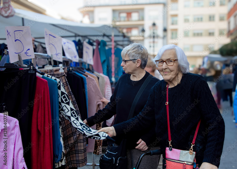 Two middle-aged women looking at clothes being sold at a flea market Two middle-aged women looking at clothes being sold at a flea market