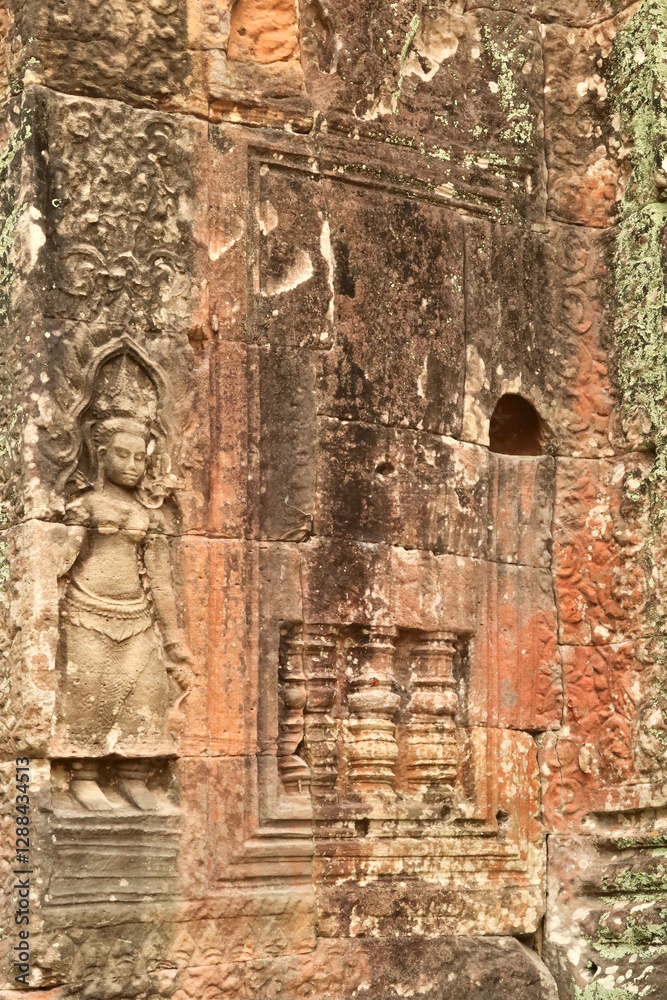 An apsara is carved into a wall overgrown with red, green, orange moss, lichens at the Prasat Preah Khan Temple, Angkor Wat, Siem Reap, Cambodia An apsara is carved into a wall overgrown with red, green, orange moss, lichens at the Prasat Preah Khan Temple, Angkor Wat, Siem Reap, Cambodia