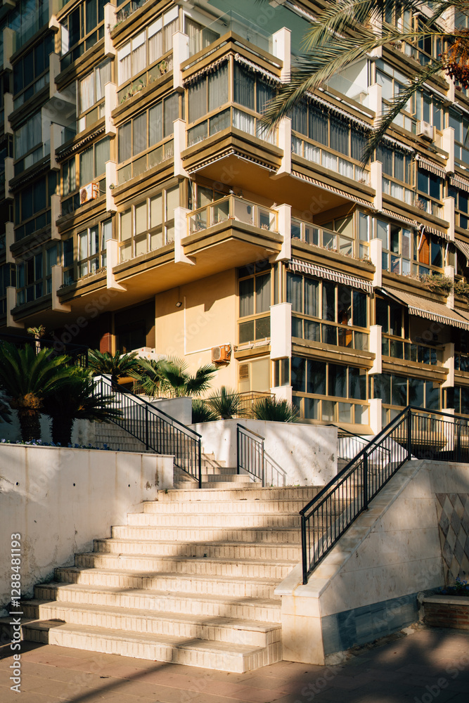 An outdoor staircase illuminated by sunlight with palm shadows on the steps, leading up to an apartment building facade An outdoor staircase illuminated by sunlight with palm shadows on the steps, leading up to an apartment building facade