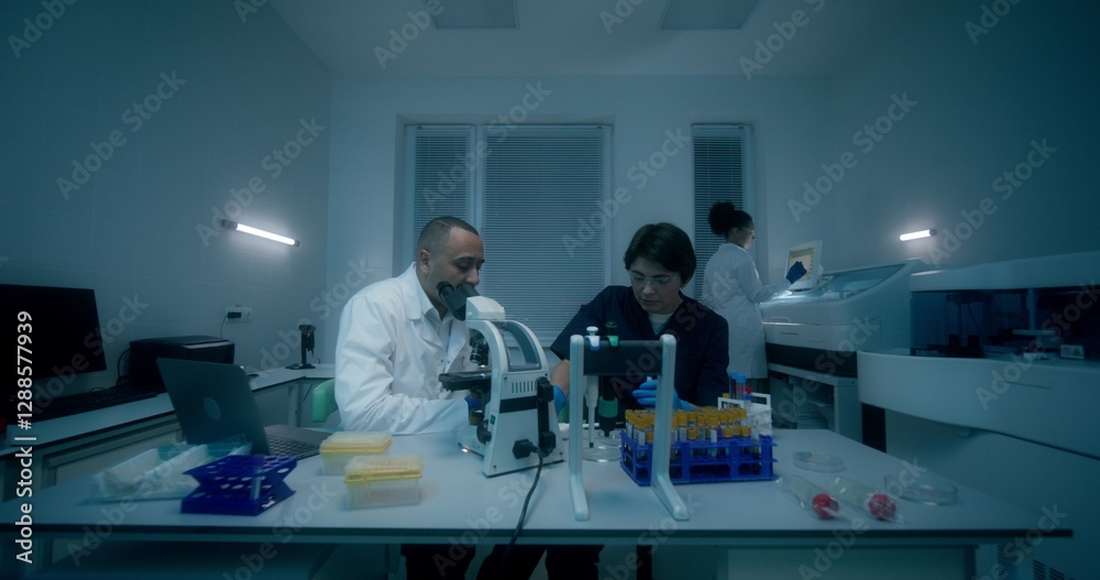 Naklejka premium A group of laboratory assistants in medical clothes work in a medical laboratory, using a microscope and conducting a blood test