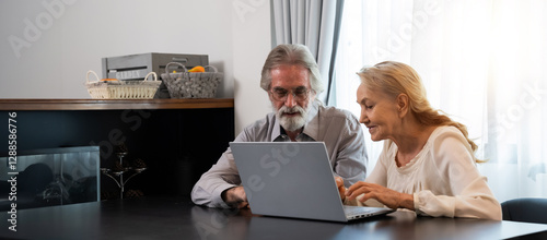 Happy Caucasian 70s mature couple using laptop at home. Old people using computer at home. Senior man and woman surfing the web on a wireless laptop connection. Modern retired lifestyle people.