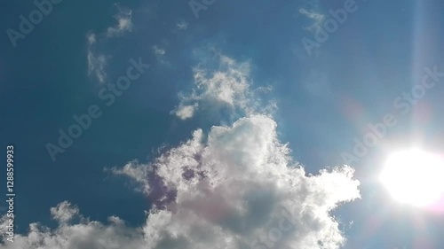 Blue sunny sky, sun, sunrays and slowly moving white clouds in nice and calm weather. Topics: cloudscape, sky space, meteorology, season, air space, sun energy, sunlight, season