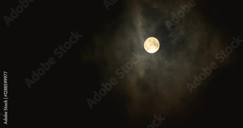 The full moon shines through the clouds in a dark night sky