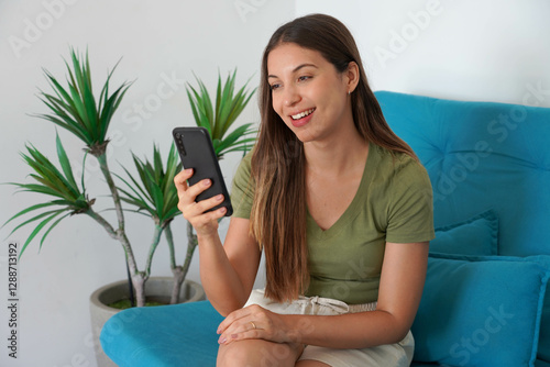 Bild auf Leinwand Brazilian girl using smartphone app for chat on her couch at home