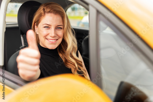 Obraz na płótnie A confident blonde woman sits in a yellow car, smiling and giving a thumbs-up through the window, symbolizing success, happiness, and independence. w salonie