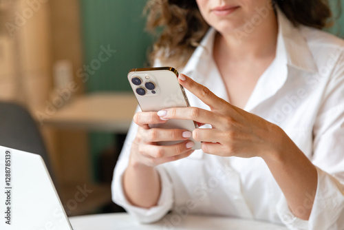 Young woman use cellphone, sit at table, share text messages in social media, enjoy new vlog, watch internet content take break from work on laptop. Tech, e-services, mobile app usage concept