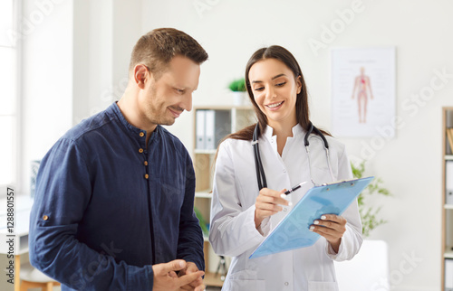 Portrait of a young man patient in medical office listening to a friendly female doctor holding report file with appointment and giving consultation during medical examination in clinic.