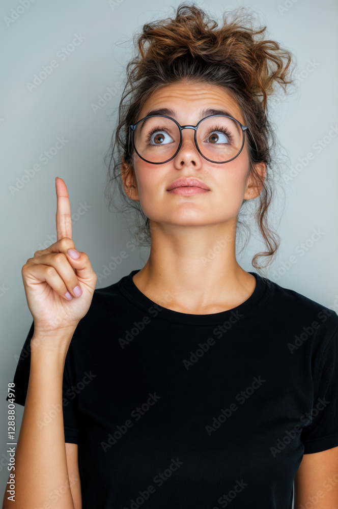 Jeune femme avec lunettes et chignon désordonné pointant vers le haut avec un regard d'eurêka Jeune femme avec lunettes et chignon désordonné pointant vers le haut avec un regard d'eurêka