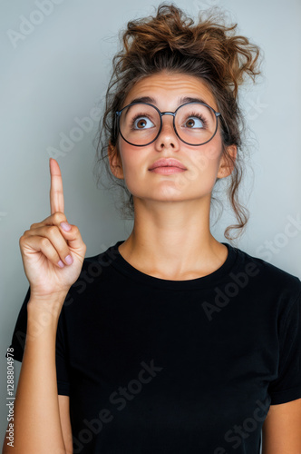 Jeune femme avec lunettes et chignon désordonné pointant vers le haut avec un regard d'eurêka