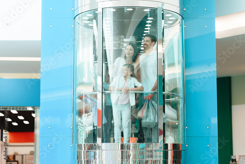 Father, mother and daughter are going down in elevator in shopping mall.