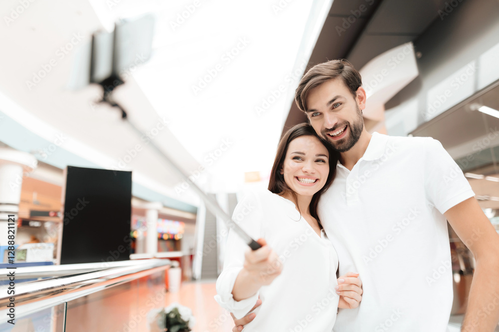 Man and woman in shopping mall. Couple is taking selfie with selfie stick.