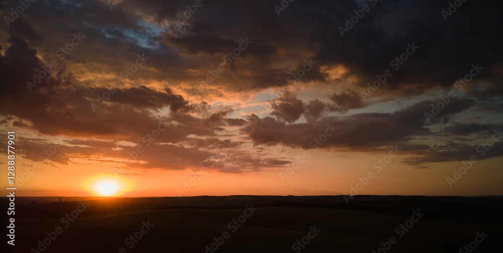 Bright colorful sunset sky with setting sun and vibrant clouds over dark landscape Bright colorful sunset sky with setting sun and vibrant clouds over dark landscape