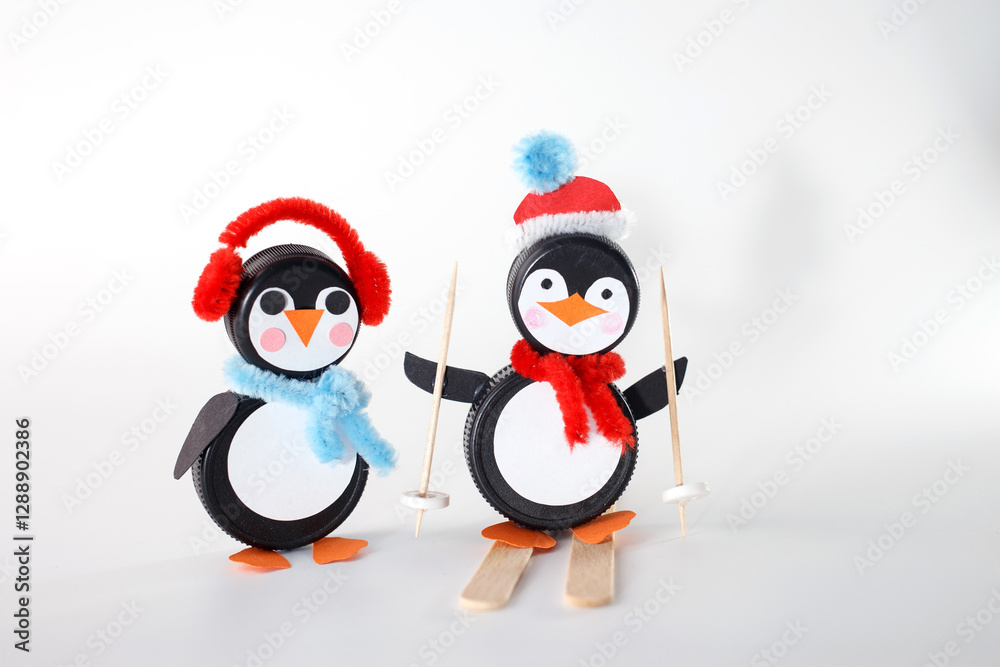 Fototapeta premium Penguin crafts made from bottle caps, dressed in festive accessories like earmuffs and Santa hats. Ideal for businesses focusing on holiday crafts, upcycling materials, and winter-themed DIY projects.