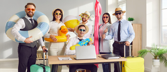 Happy business team ready for their summer vacation together. Group of cheerful, smiling coworkers with holiday bags, funny beach toys, sun hats and sunglasses by desk in office workplace
