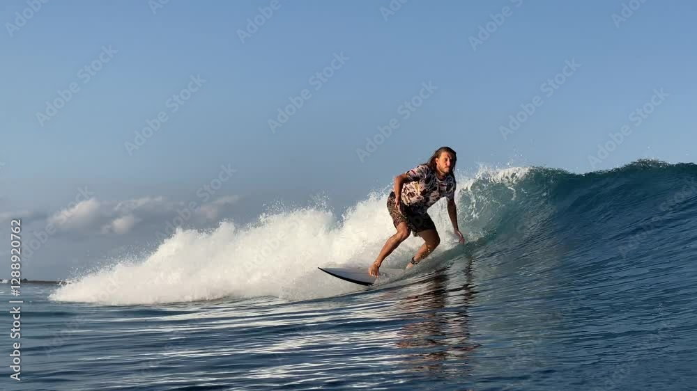 Long-haired man surfer catches a wave in the ocean and rides on it, makes turns. Blue Wave in the Indian Ocean.Bali.Indonesia Long-haired man surfer catches a wave in the ocean and rides on it, makes turns. Blue Wave in the Indian Ocean.Bali.Indonesia