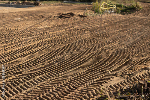 photo Close-up view of intricately patterned tire tracks imprinted on the sandy terrain at a construction site, revealing the heavy machinery's movement and landscaping work
