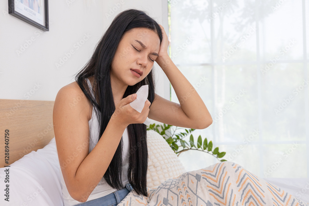 Woman sneezing into tissue while sitting in bed Woman sneezing into tissue while sitting in bed