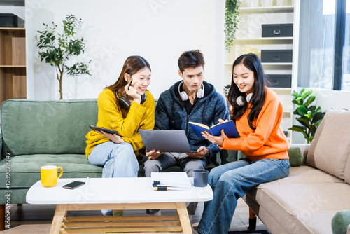 Three Asian young adult students sit in university living room, discussing their study abroad experiences, academic research, preparing thesis report, planning future global education opportunities.