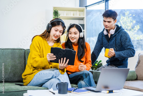 Three Asian young adult students sit in university living room, discussing their study abroad experiences, academic research, preparing thesis report, planning future global education opportunities.