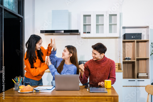 Three Asian young adult students sit around the kitchen table, attending online class on tablet. They engage in video conferencing, discussing lessons, taking notes, digital learning experience. photo